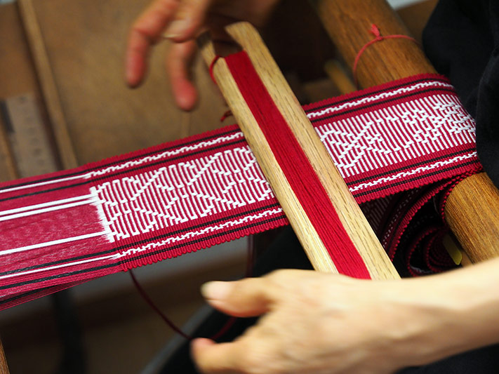 Close-up of the weaver's hands as she makes the red and white obi sash.